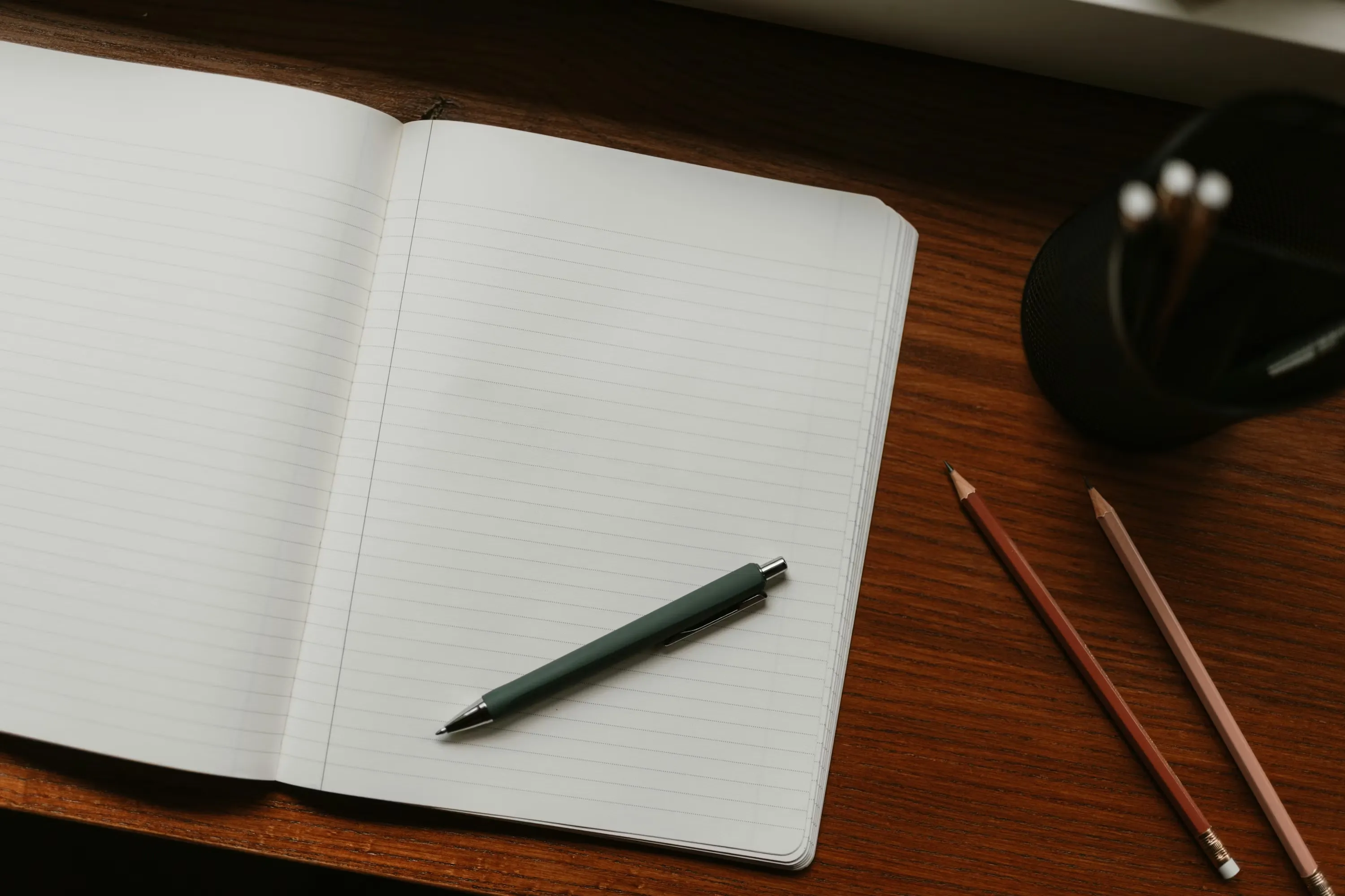A journal open on a wooden desk with a warm lamp, a pen resting on the page, and soft evening light through a window
